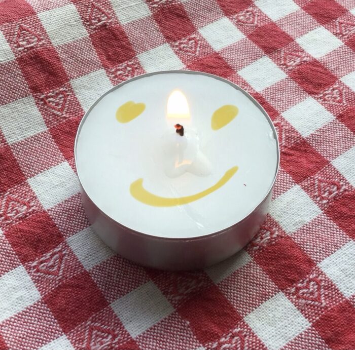 Waxinelichtje dat brandt met daarop een smiley getekend.